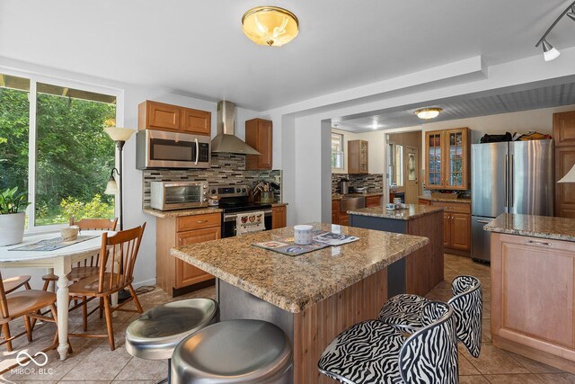 kitchen featuring light tile patterned flooring, wall chimney exhaust hood, a center island, appliances with stainless steel finishes, and backsplash