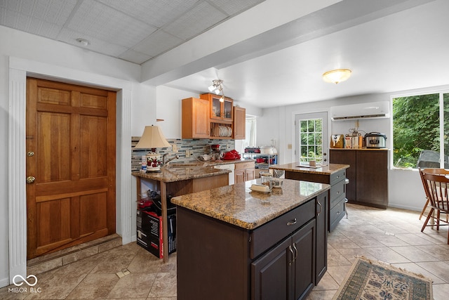 kitchen featuring a wall unit AC, white dishwasher, a center island, light stone counters, and light tile patterned floors