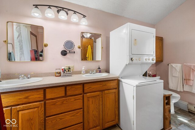 bathroom featuring a textured ceiling, tile patterned floors, toilet, stacked washing maching and dryer, and double sink vanity