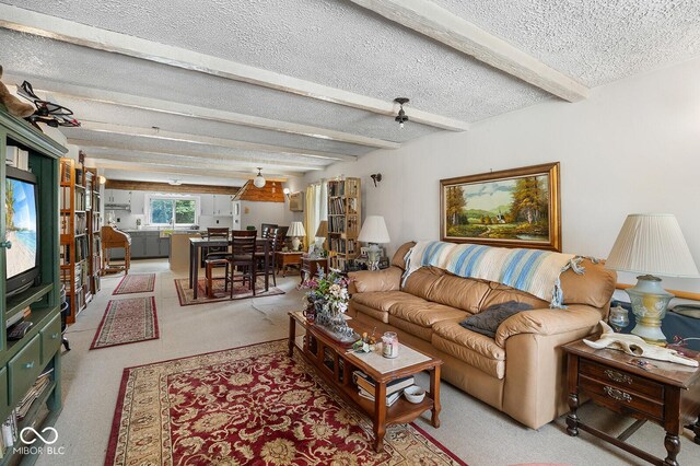 living room with ceiling fan, beamed ceiling, light carpet, and a textured ceiling