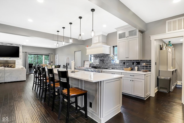 kitchen with a center island with sink, a breakfast bar, custom exhaust hood, and dark hardwood / wood-style floors