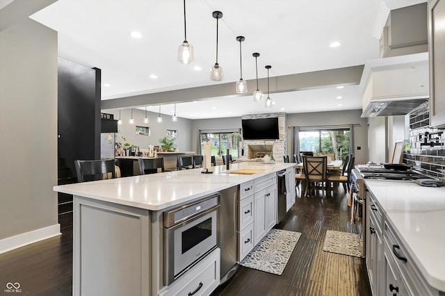 kitchen with appliances with stainless steel finishes, an island with sink, gray cabinets, and dark wood-type flooring