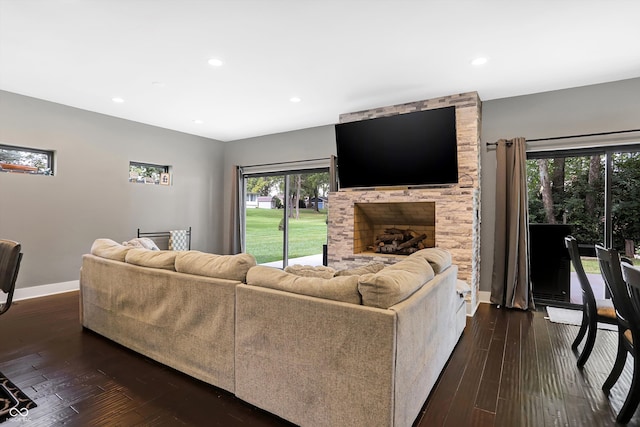 living room with plenty of natural light, a stone fireplace, and dark hardwood / wood-style floors