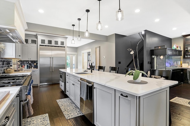 kitchen with a breakfast bar, custom range hood, decorative backsplash, high end appliances, and a center island with sink