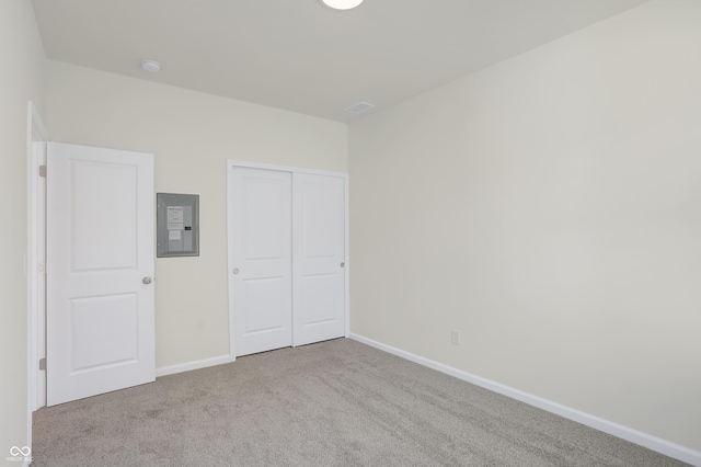 unfurnished bedroom featuring electric panel, a closet, and light colored carpet