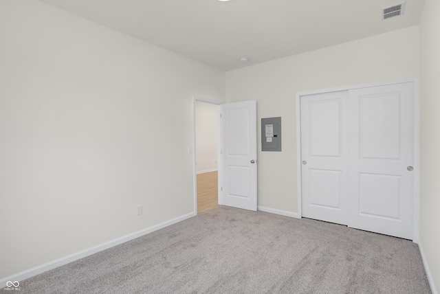 unfurnished bedroom with light carpet, electric panel, and a closet