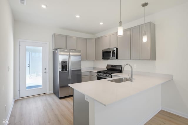 kitchen featuring sink, hanging light fixtures, light hardwood / wood-style floors, kitchen peninsula, and stainless steel appliances