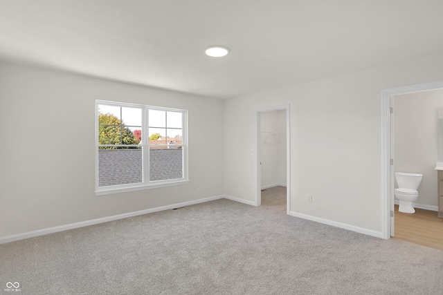 unfurnished bedroom with a walk in closet, ensuite bathroom, a closet, and light colored carpet