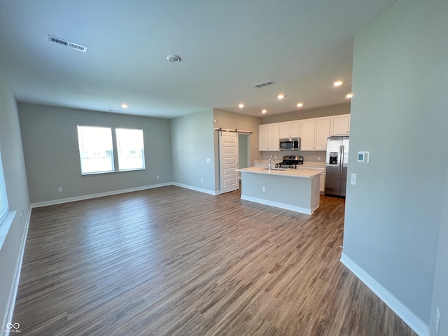 kitchen featuring appliances with stainless steel finishes, a barn door, hardwood / wood-style floors, and white cabinetry