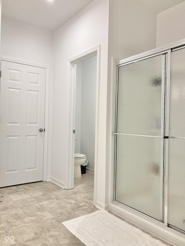 bathroom featuring a stall shower, toilet, and baseboards