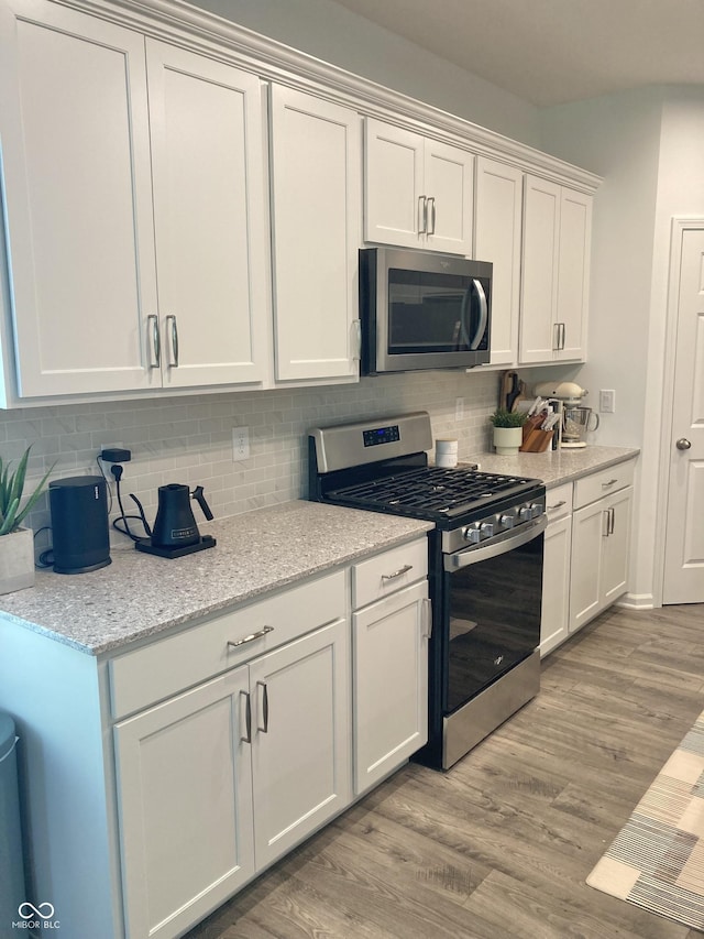 kitchen with stainless steel appliances, white cabinetry, light wood-style floors, and light stone counters