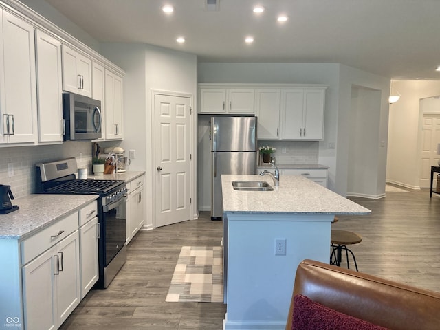 kitchen with stainless steel appliances, white cabinetry, a sink, and an island with sink