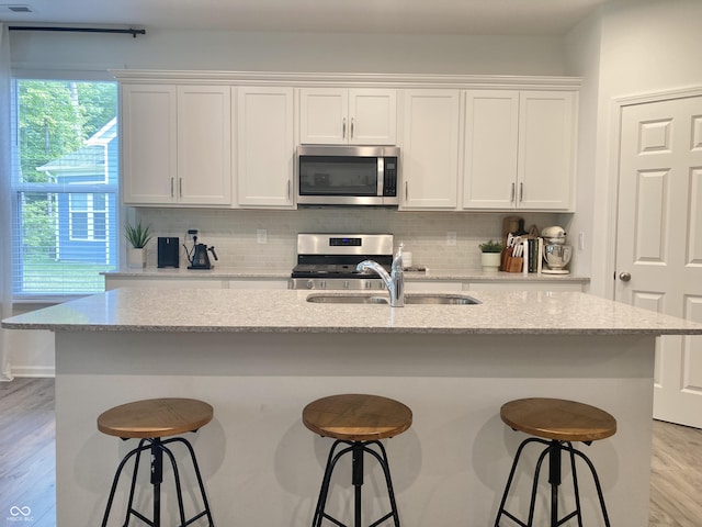 kitchen featuring a kitchen island with sink, appliances with stainless steel finishes, white cabinetry, and light stone countertops