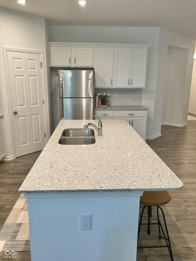 kitchen featuring a sink, white cabinetry, freestanding refrigerator, light stone countertops, and a center island with sink