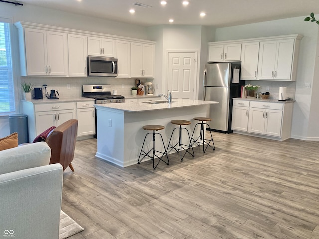 kitchen featuring white cabinets, appliances with stainless steel finishes, a breakfast bar, a kitchen island with sink, and a sink