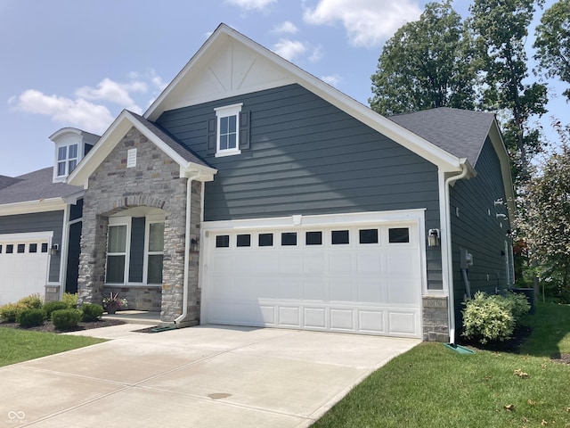 craftsman inspired home featuring a shingled roof, a front yard, a garage, stone siding, and driveway