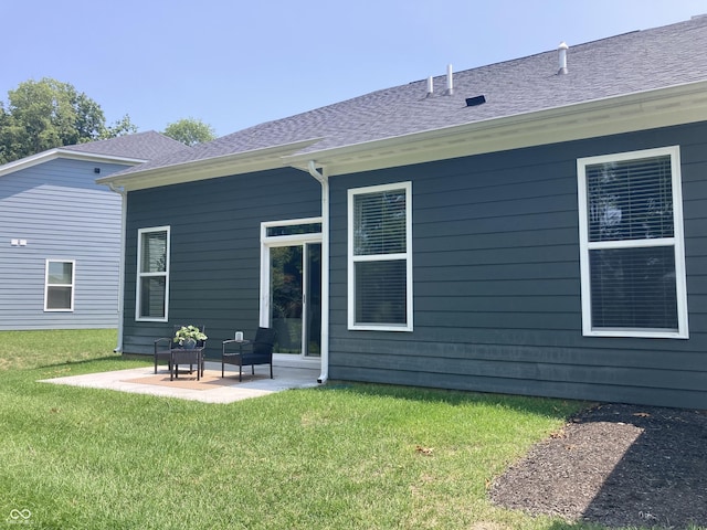 back of property featuring a shingled roof, a lawn, and a patio area