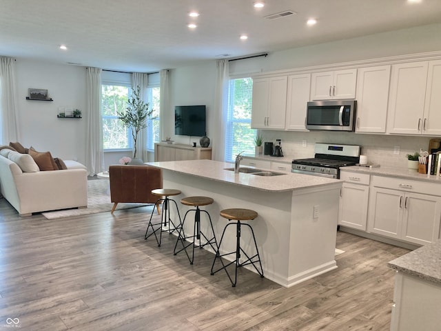 kitchen with open floor plan, stainless steel appliances, a kitchen island with sink, and white cabinets