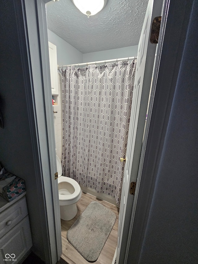 bathroom featuring a textured ceiling, curtained shower, hardwood / wood-style flooring, and toilet