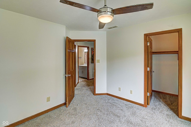 unfurnished bedroom with ceiling fan, a spacious closet, light carpet, and a closet