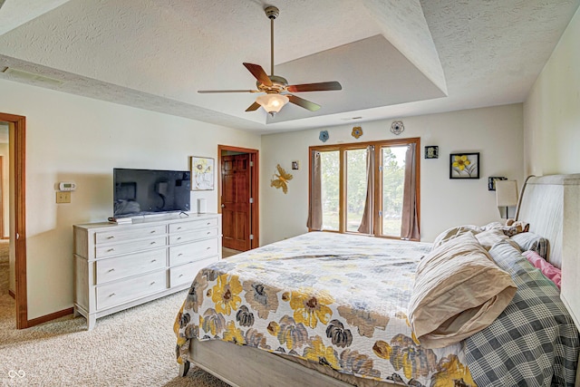 carpeted bedroom with a textured ceiling, a tray ceiling, and ceiling fan