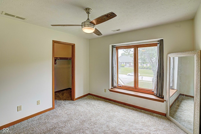 unfurnished bedroom with a textured ceiling, a walk in closet, a closet, and light colored carpet