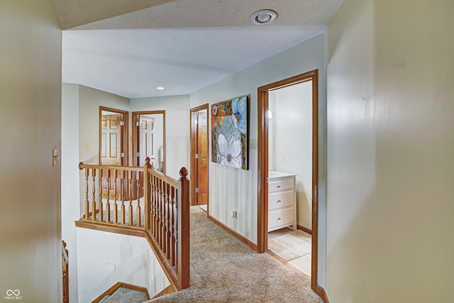 hallway with a textured ceiling and light colored carpet