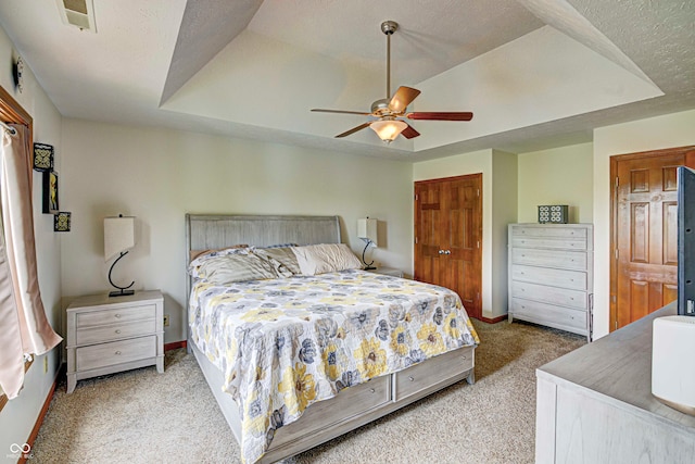 bedroom with ceiling fan, a textured ceiling, a tray ceiling, and light colored carpet