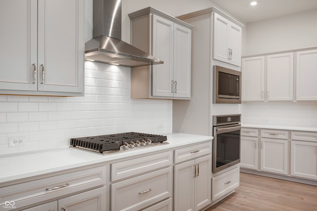 kitchen featuring appliances with stainless steel finishes, backsplash, light hardwood / wood-style floors, and wall chimney exhaust hood