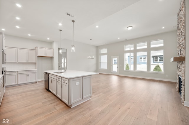 kitchen with a stone fireplace, white cabinetry, a center island with sink, and light hardwood / wood-style floors