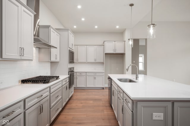 kitchen featuring appliances with stainless steel finishes, wall chimney exhaust hood, sink, pendant lighting, and light hardwood / wood-style floors