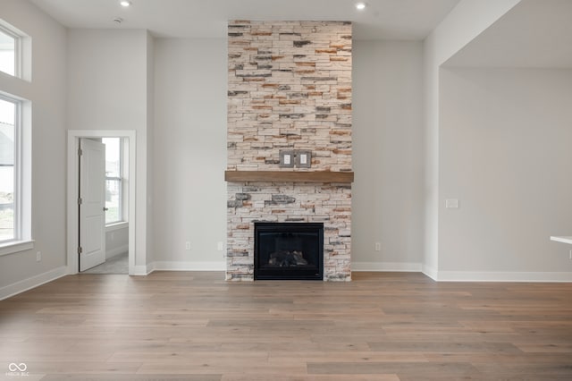 unfurnished living room featuring a stone fireplace, a wealth of natural light, and light hardwood / wood-style floors