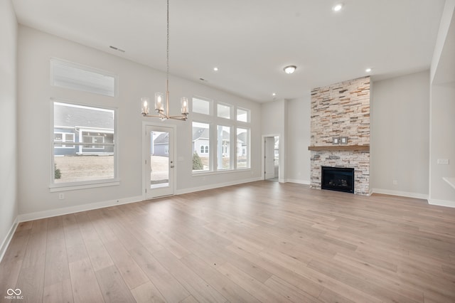 unfurnished living room with a stone fireplace, a notable chandelier, and light wood-type flooring