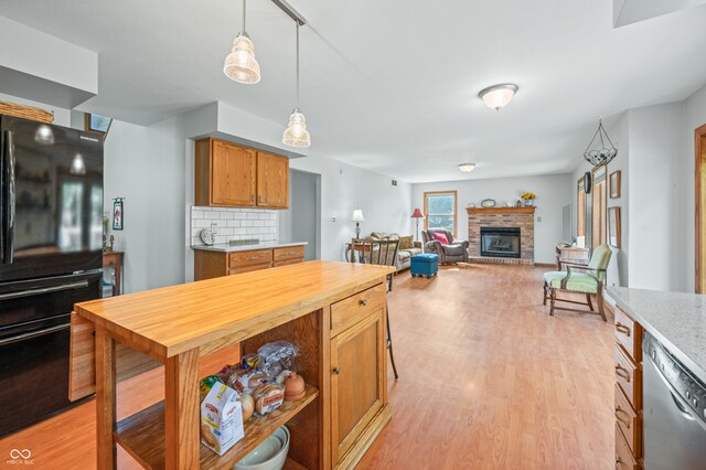 kitchen with dishwasher, decorative backsplash, decorative light fixtures, light wood-type flooring, and a fireplace