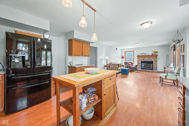 kitchen featuring light wood-type flooring, a fireplace, backsplash, black fridge, and hanging light fixtures