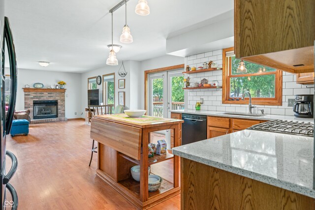 kitchen with dishwasher, decorative backsplash, sink, a brick fireplace, and light wood-type flooring