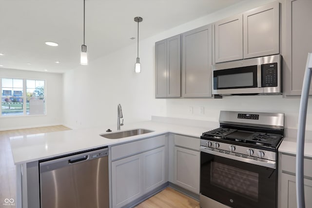 kitchen featuring stainless steel appliances, sink, gray cabinetry, and decorative light fixtures