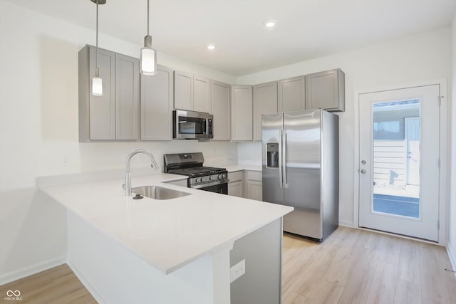 kitchen featuring sink, light hardwood / wood-style flooring, appliances with stainless steel finishes, kitchen peninsula, and pendant lighting