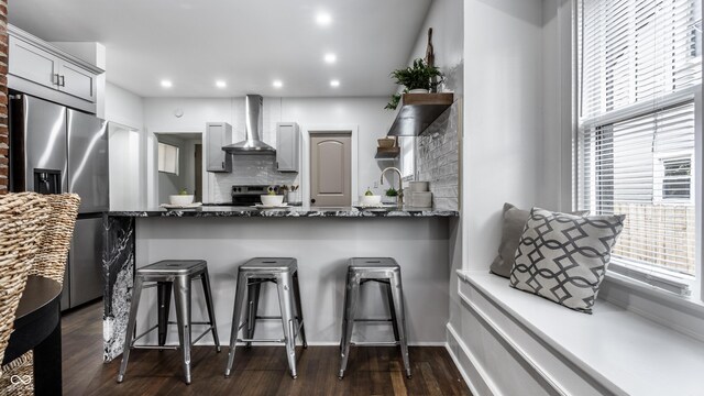 1210 Finley Ave, Indianapolis, IN 46203 - kitchen with wall chimney range hood, stainless steel appliances, tasteful backsplash, dark stone counters, and a kitchen breakfast bar