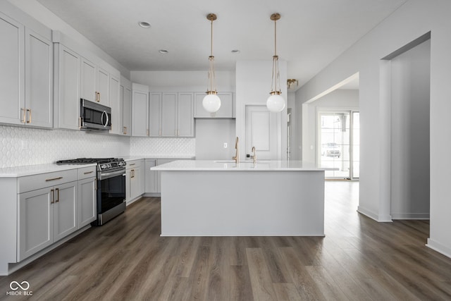 kitchen featuring decorative light fixtures, dark wood-type flooring, tasteful backsplash, a kitchen island with sink, and stainless steel appliances