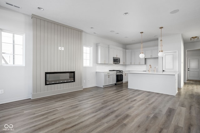 kitchen with decorative light fixtures, white cabinets, a center island, a large fireplace, and stainless steel appliances