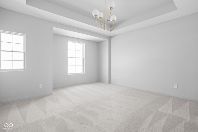 carpeted spare room with a notable chandelier and a raised ceiling