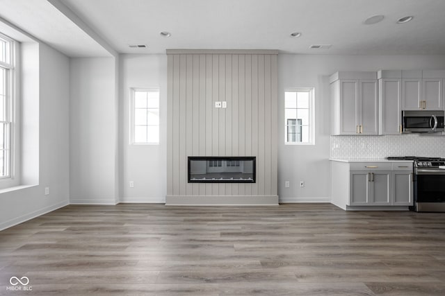 unfurnished living room with a large fireplace, light wood-type flooring, and a healthy amount of sunlight