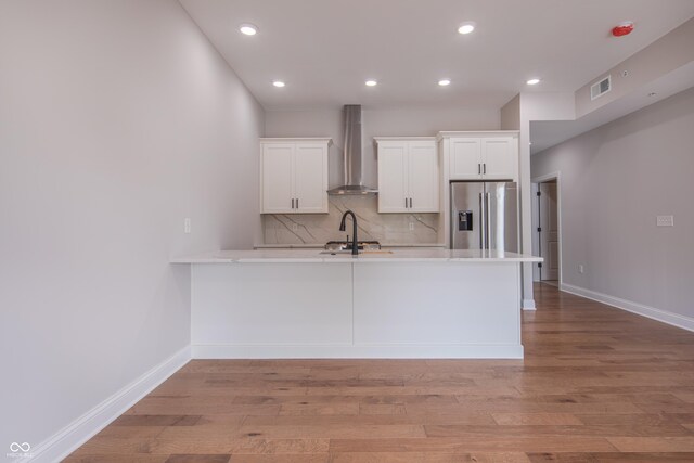 kitchen featuring stainless steel fridge, wall chimney range hood, tasteful backsplash, and light hardwood / wood-style flooring