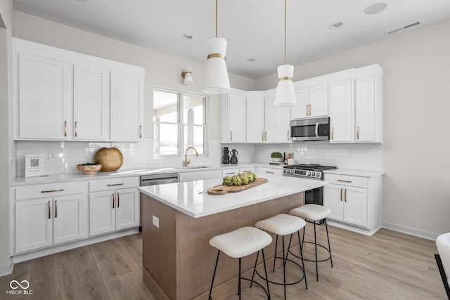 kitchen with a kitchen island, a kitchen bar, white cabinetry, stainless steel appliances, and hanging light fixtures