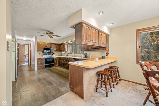 kitchen featuring kitchen peninsula, a breakfast bar, a textured ceiling, white range with electric stovetop, and hardwood / wood-style flooring