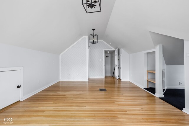 bonus room featuring a notable chandelier, light wood-type flooring, built in features, and vaulted ceiling