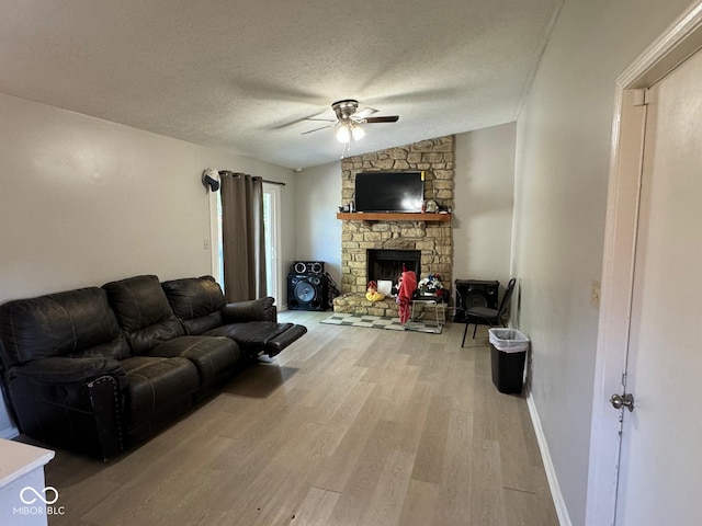 living room featuring a textured ceiling, a stone fireplace, light hardwood / wood-style floors, ceiling fan, and vaulted ceiling