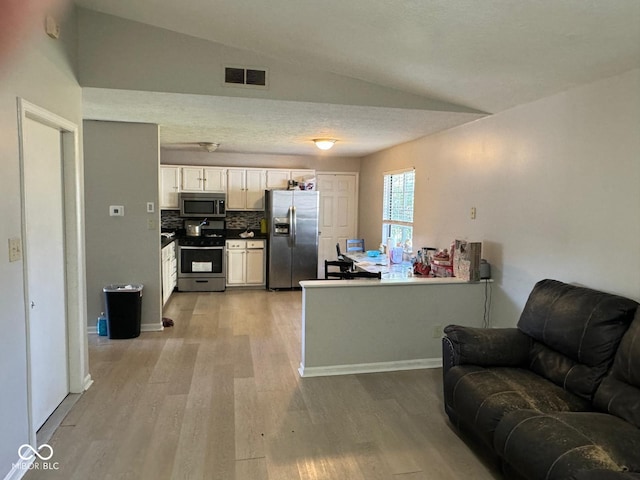 kitchen featuring appliances with stainless steel finishes, white cabinetry, lofted ceiling, decorative backsplash, and light hardwood / wood-style floors