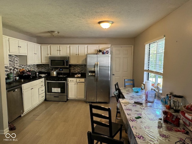 kitchen with sink, white cabinetry, tasteful backsplash, light hardwood / wood-style flooring, and appliances with stainless steel finishes